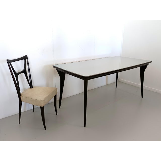 Made in Italy, 1950s. This dining table features an ebonized beech frame and its original back-painted pale green glass...