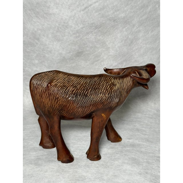 Decorative hand-carved wooden buffalo figurine. The textured surface and simplified, organic form indicate traditional...