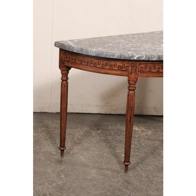 A beautifully carved French demi-lune wood table with marble top from the early 19th century. This antique console table...