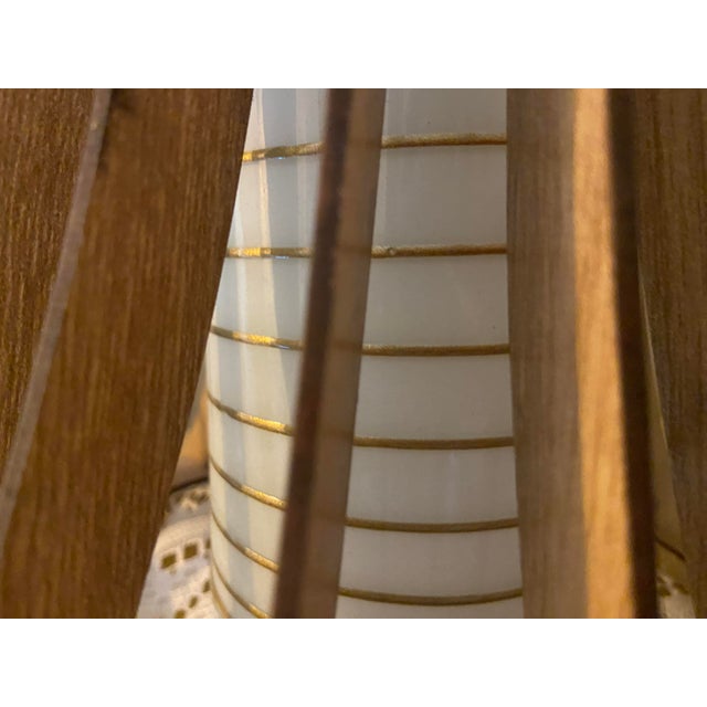 A striking sculptural pendant light combining natural wood tones with elegant white glass and gold detailing. This...