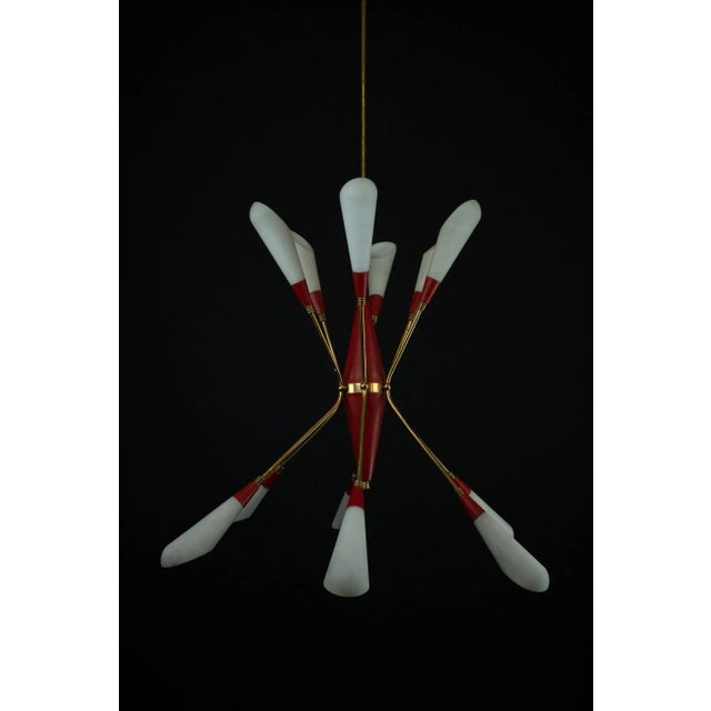 Mid-Century 12-light chandelier in the manner of Stilnovo, Italy, 1950s. Featuring a brass structure with red lacquered...