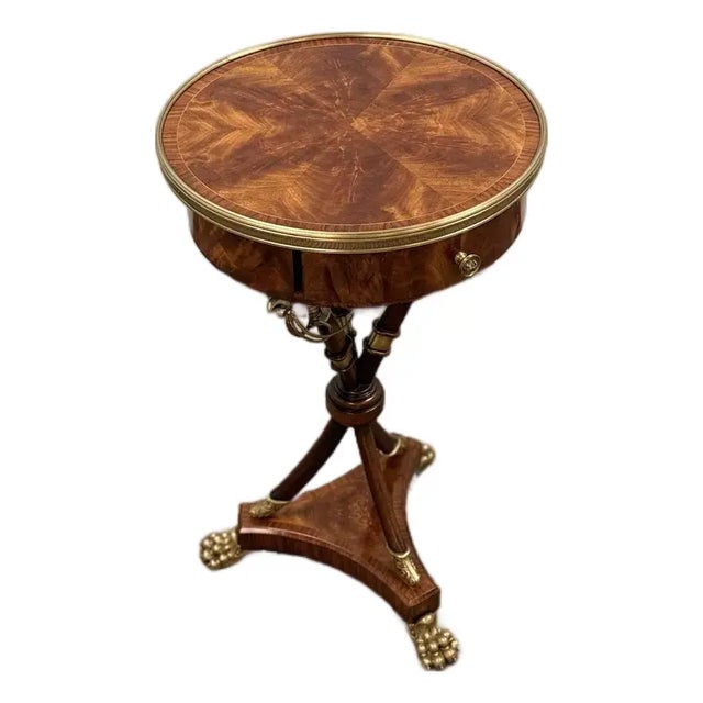 Elegant round pedestal accent table featuring rich wood veneer, a brass gallery edge, and tripod base with brass claw...