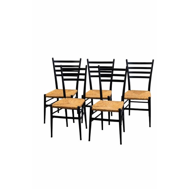 Set of 5 Italian ladder-back dining chairs dating to the 1960s. The chairs feature slender black-painted wood frames with...