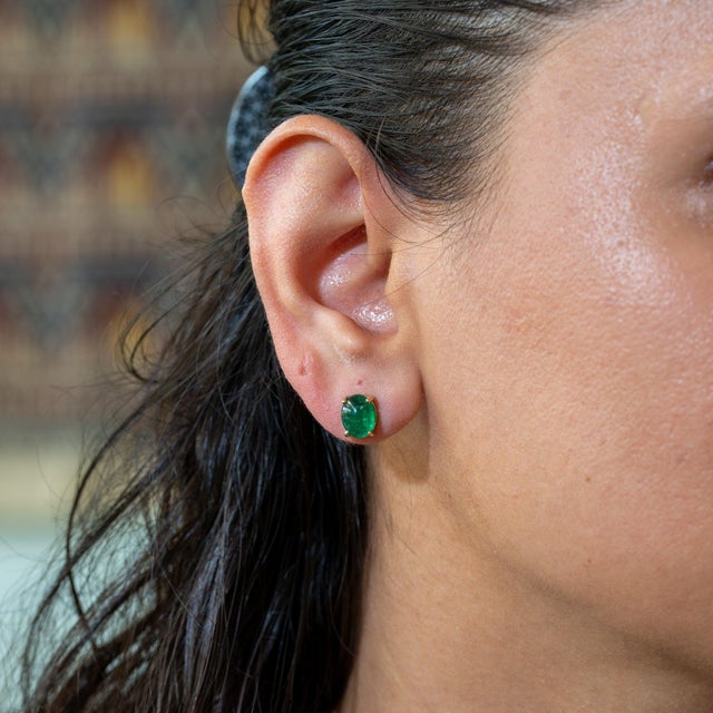 A matched pair of Zambian emerald cabochons glows in deep, saturated green in these solid 14K yellow gold solitaire stud...
