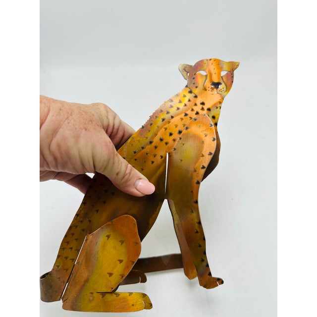 This is a stylized metal cheetah sculpture made from cut and hand-painted sheet metal pieces. The figure shows a sitting...