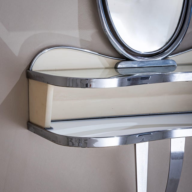Wall-mounted console featuring a tilting oval mirror and two shelves with gracefully curved outlines. The shelf edges and...