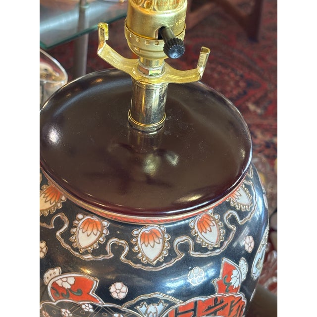 Elegant Chinoiserie style table lamp in hues of black, red, yellow, white and gold. Classical ginger jar shape on wood base