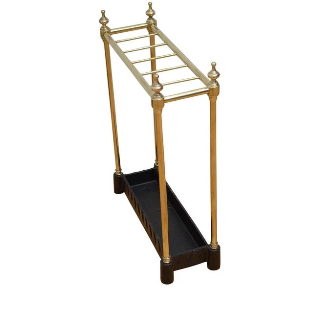 An English umbrella stand in brass with six divisions flanked by decorative finials and cast iron drip tray with dogtooth...