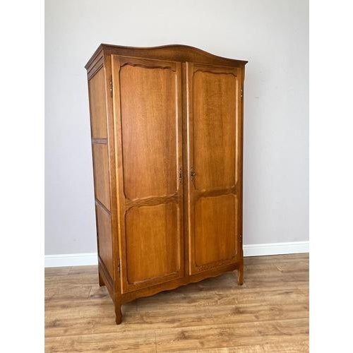 An elegant Vintage French Louis wardrobe in oak, featuring a warm finish, gently shaped cornice, panelled double doors and...