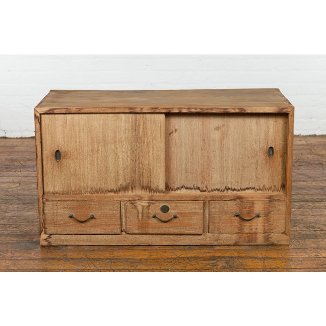 An antique Japanese low storage cabinet from the early 20th century, with sliding doors, three drawers and metal hardware....