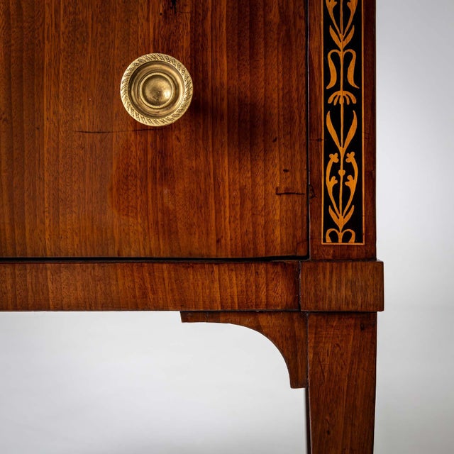 Compact neoclassical chest of drawers with two drawers, bronze fittings and tall tapered legs. The pilaster strips of the...
