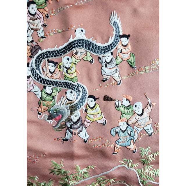 A large and visually striking antique Chinese silk embroidered panel depicting a lively dragon dance scene, with finely...