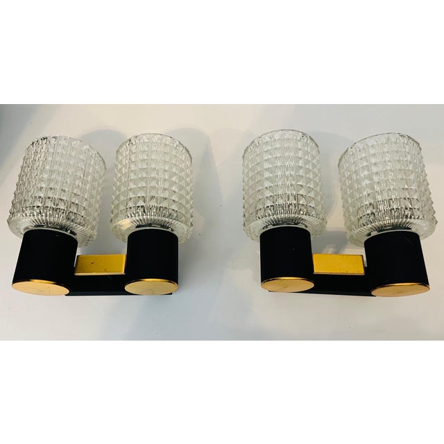 An original pair of French 1960s sconces composed of golden polished brass and black enamel fixtures with cut crystal...