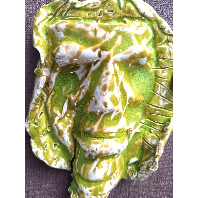 Painting with green glazed ceramic mask, featuring the stylized face of a man with deep eyes. The artefact is worked...
