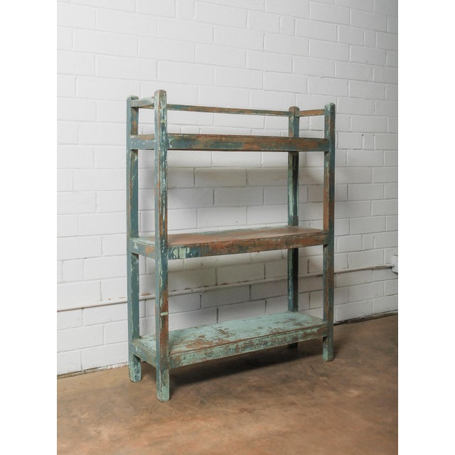 This wooden shelving unit features a straightforward, utilitarian form highlighted by its original blue-green painted...