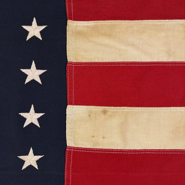 This vintage American flag is made from a cotton cloth with fully sewn stars and stripes. Please note overall staining and...