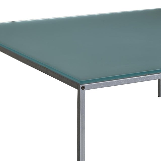 A square coffee table with a minimalist and elegant design, featuring a simple metal frame and a top in blue sandblasted...
