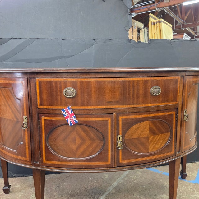 This English Bowfront Mahogany Satin Banded Sheraton Style Sideboard on tapered legs with spade feet is a beautiful...