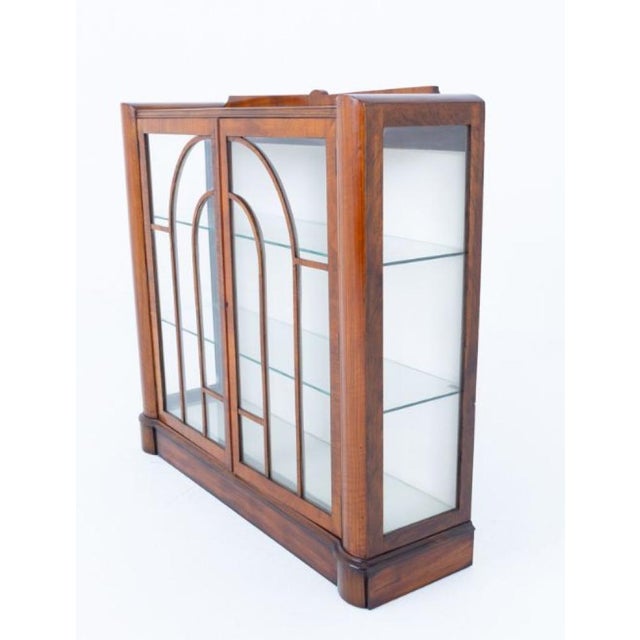 A stylish Art Deco walnut display cabinet, standing on a shaped plinth base and exhibiting the clean lines and elegant...