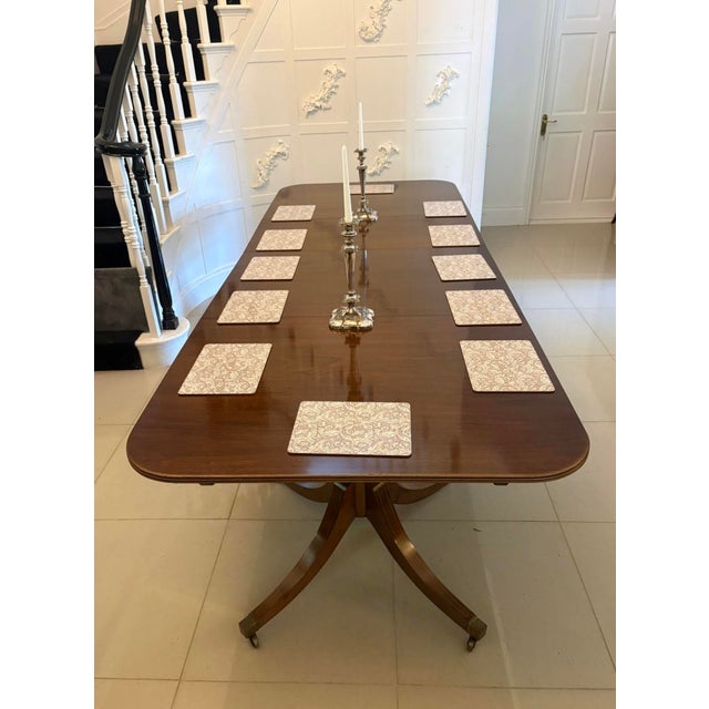 An antique English figured mahogany extending dining table in the Regency style built as a twin pillar design and seating...