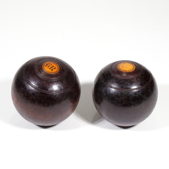 A pair of antique lignum vitae bocce lawn bowling balls (4.5” diameter) in dark stained wood with small circular inset...