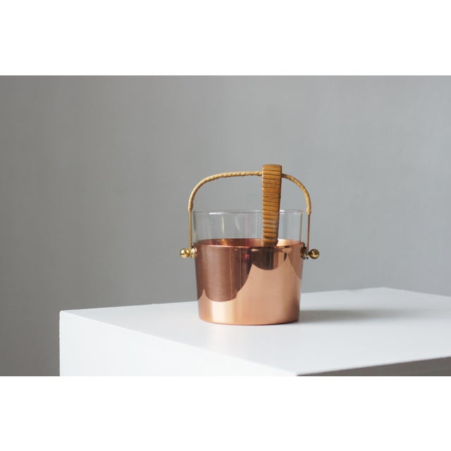 A cylindrical vessel made of polished copper, with a transparent glass insert set inside. The body is complemented by a...