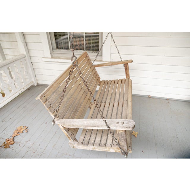 A classic porch swing, possibly teak with a traditional splatted form and flanking chain supports. Condition: With...