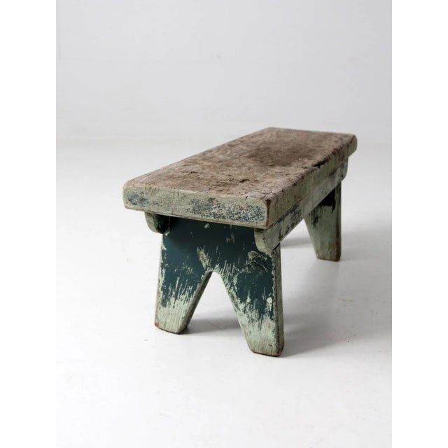 This is a primitive antique wood bench from the late 19th century. The rustic farmhouse footstool has a naturally mottled...