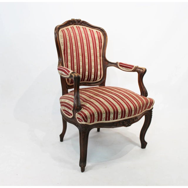 New Rococo armchair of polished wood with carvings and upholstered with striped fabric from 1890. The chair is in great...