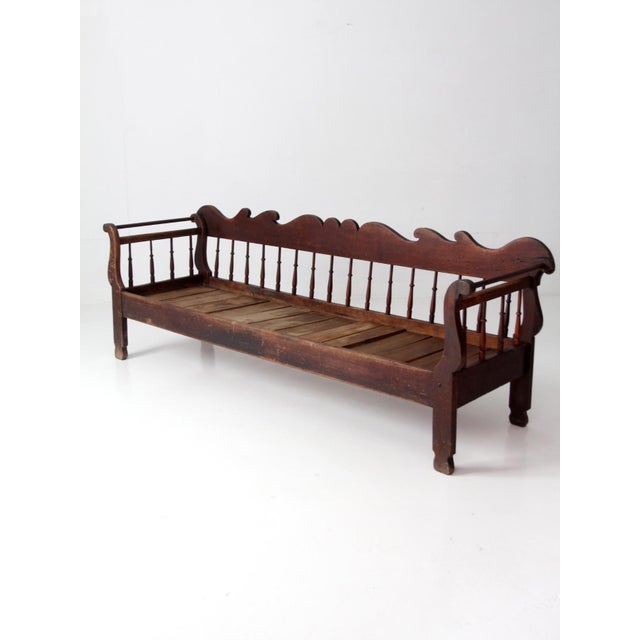 An antique 19th-century wooden bench featuring an elaborately scalloped crest rail, slender turned spindles, shaped arms,...