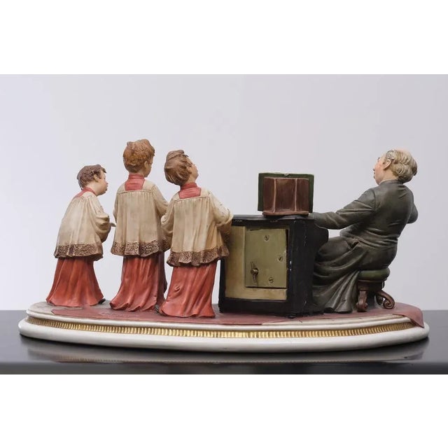 The choirboys. Three choir boys singing, directed by a priest, this Capodimonte porcelain made on a kidney shaped base....