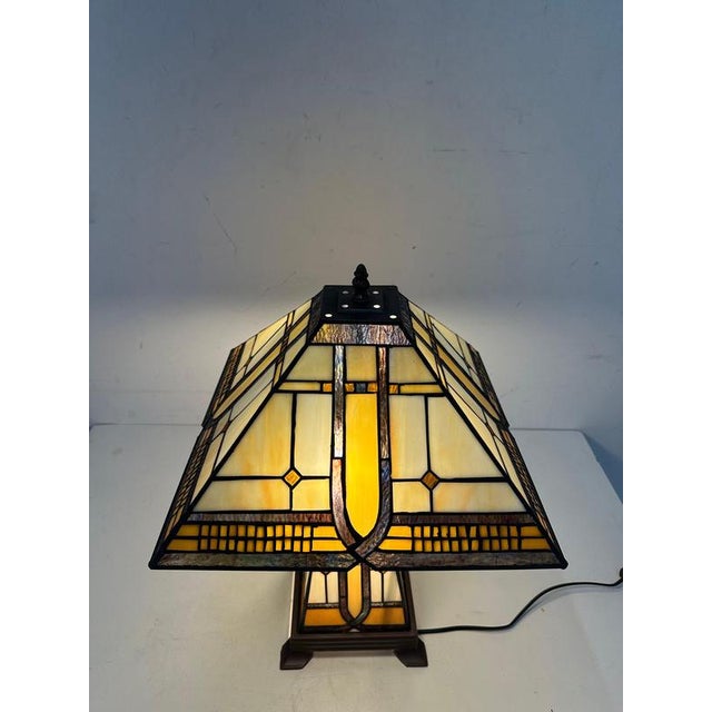 Decorative Tiffany style table lamp featuring a stained glass shade with a classic botanical motif. The shade is composed...