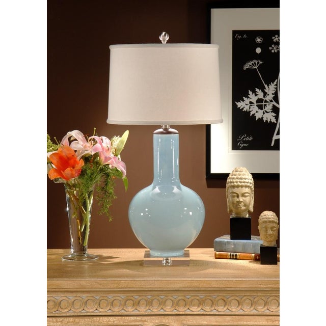 Sleek and refined, cayden lamp features a pale blue hand glazed porcelain bottle vase with a wood finished cap atop a...