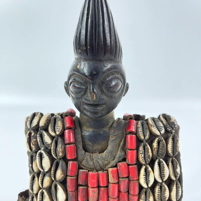 This figure is adorned in a cowrie shell vest, which is removable, and on a custom base. Ibeji figures, carved by the...