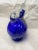 A beautiful cobalt blue tilt ball decanter with clear glass handle and clear, decorative stopper. It is adorned with a...
