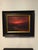 The painting captures a dramatic sunset over a meandering river, where vibrant reds and deep oranges dominate the sky,...