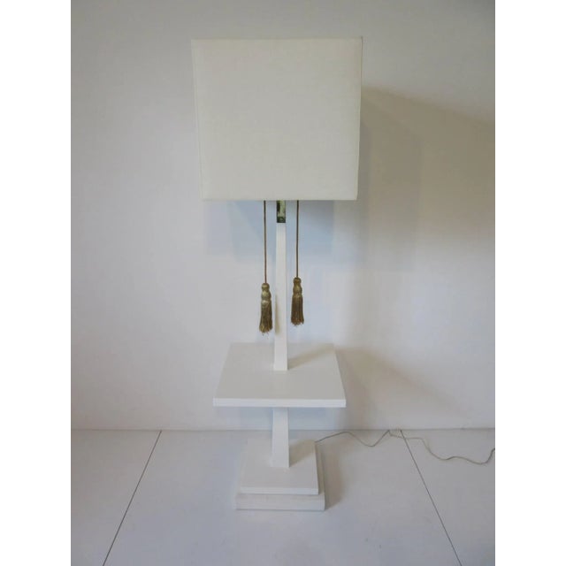 A satin white luxurious Regency styled wood floor lamp table with thick Carrara marble base and gold braided tassel lamp...
