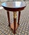 An elegant neoclassical mid-century pedestal occasional side table with a beautiful burl wood top sitting above a trio of...