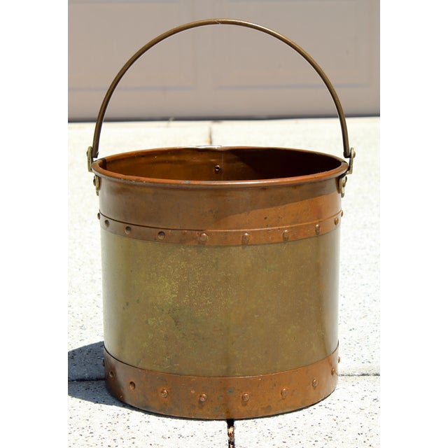 It features a classic mixed-metal construction with a brass body accented by copper bands at the top and base. The riveted...