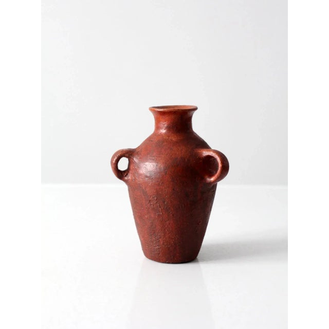 This is a vintage pottery vase. The ruddy red clay vase features three handles.