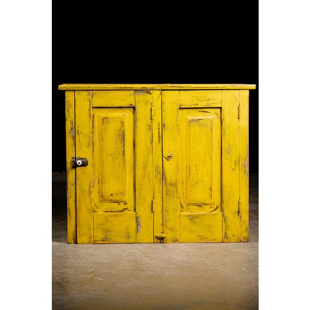 This antique cabinet features a worn yellow paint finish and an arrangement of different cubbies on the inside for the...