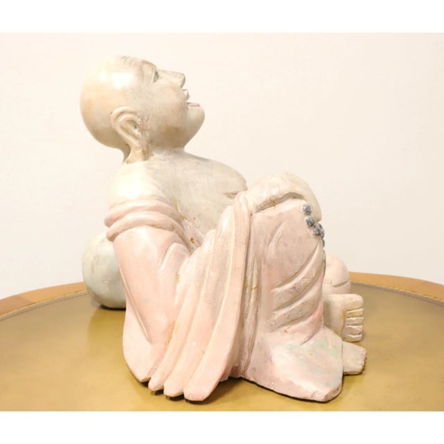 A wood carved sculpture depicting a seated smiling Buddha. Unsigned, artist unknown. Carved from a solid piece of wood and...