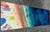 This painting by Joe Davis, is an acrylic on canvas artwork showcasing a top-down view of people on a sandy shore and in...