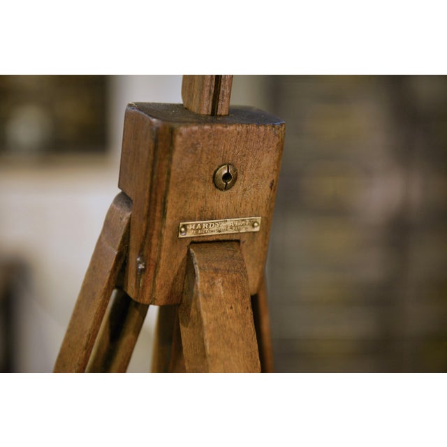 An elegant folding painter's easel with a tripod frame made of wood (probably beech) and steel hardware. The head features...