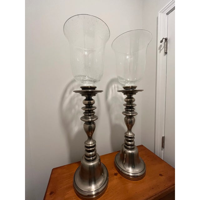 Pair of matching Chapman Hurricane Lamps. These are floor-based candleholders with speckled glass globes as shown. The...