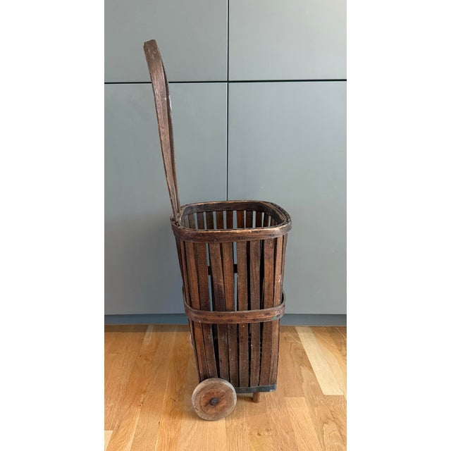 Antique rustic bentwood basket shopping cart featuring vertical wood slat body, wooden wheels and a wood handle....