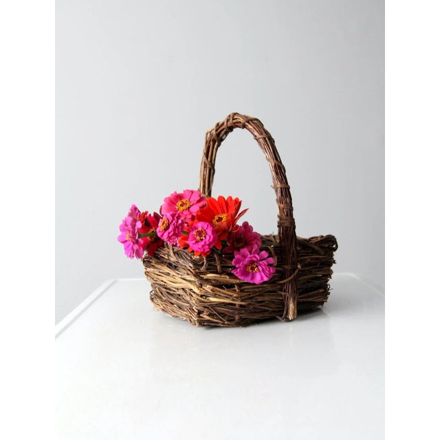 A vintage rustic woven basket crafted from natural twigs, showcasing a timeworn, organic character. The form is sturdy and...