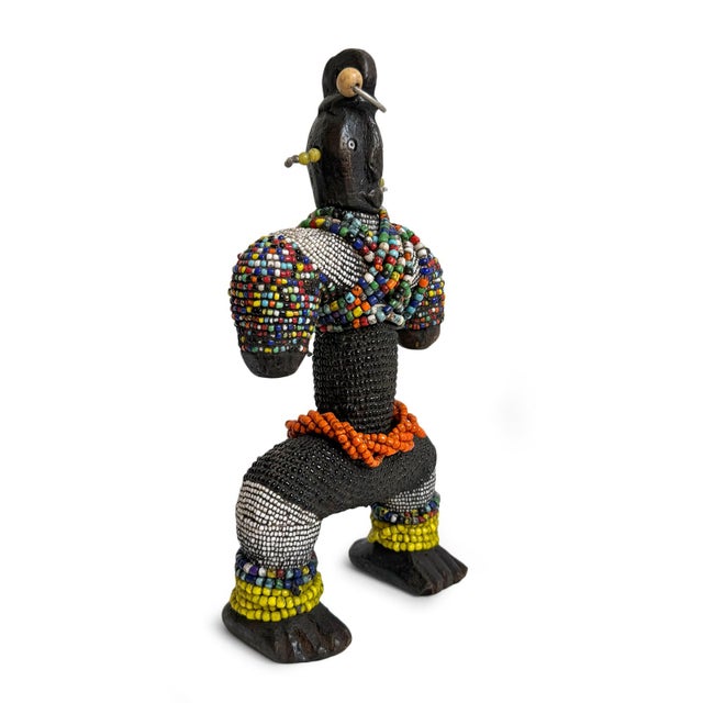 Carved vintage wooden Nigerian doll adorned with intricate beadwork in a vibrant palette of ivory, black, orange, yellow,...