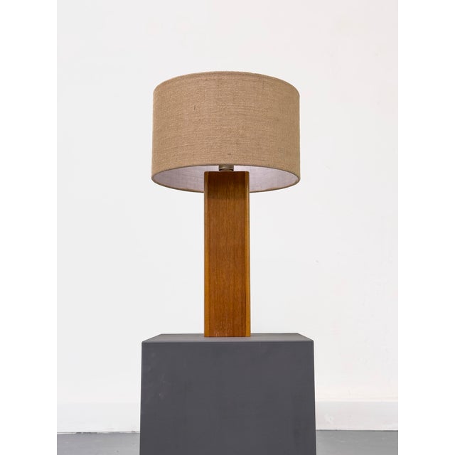 Decorative table lamp consisting of a teak wood base and a shade made of natural woven material. Includes a cable with a...
