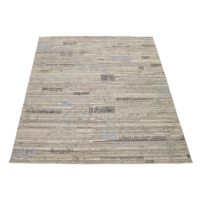 This hand-knotted wool rug features a luxurious beige base with a light brown and gray geometric pattern inspired by...